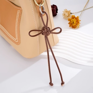 Close-up of leather bow tassel charm with golden ring on a textured crossbody bag