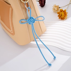 Detail of blue leather knot pendant on cream handbag with contrast stitching and metal ring