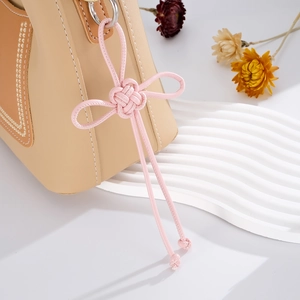 Close-up of pink handmade woven lucky knot charm on a beige handbag with soft lighting