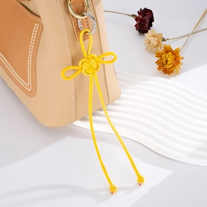 Close-up of yellow hand-woven knot pendant on a bicolor leather bag with gold hardware