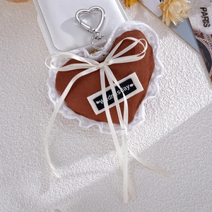Detail of a brown denim heart bag charm featuring white lace trim and a silver clasp
