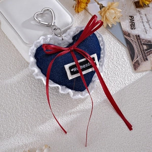 Detailed close-up of a denim heart bag charm with white lace edges and a red silk bow