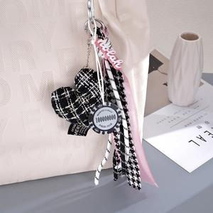 Close-up of heart charm with pink ribbon and poker chip tag on a beige handbag