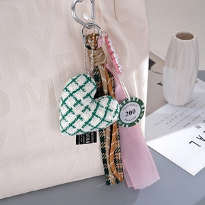 Green tweed heart charm with woven rope, pink ribbon, and poker chip on a white bag