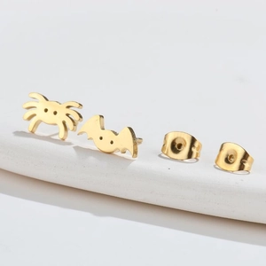 Macro detail of asymmetric gold bat and spider stud earrings for Halloween punk style