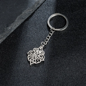 Silver stainless steel keychain with elegant filigree flower pendant on dark leather surface
