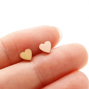 Vue rapprochée de petites boucles d'oreilles cœur dorées tenues par un doigt