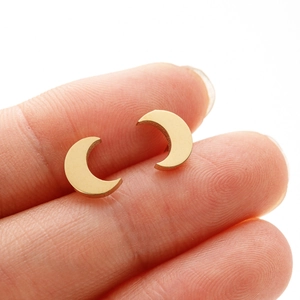 Gros plan détaillé de petites boucles d'oreilles lune dorées posées sur le bout du doigt