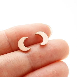 Vue macro détaillée de petites boucles d'oreilles lune en or rose sur le bout d'un doigt