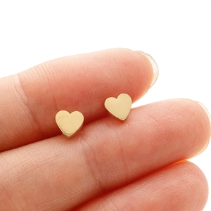 Macro detail of minimalist polished gold heart studs showing size scale on a finger