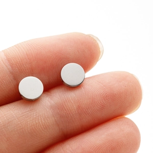Macro detail of small polished silver stainless steel disc stud earrings held by hand