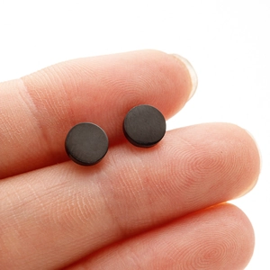 Minimalist matte black round stud earrings for men and women shown on fingers