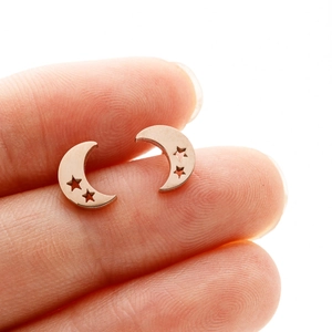 Close-up of rose gold moon and star studs held between fingers to show scale