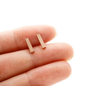 Gros plan de boucles d'oreilles rectangulaires minimalistes en or rose sur un doigt