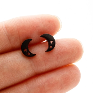 Macro detail of matte black moon stud earrings with star cutouts held on fingertip