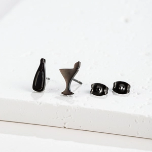 Macro shot of asymmetrical black wine bottle and martini glass stud earrings on stone base