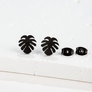 Detail of matte black monstera leaf earrings with butterfly backs on white stone base