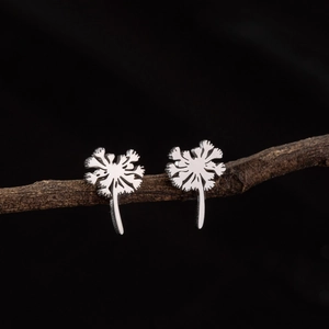 Macro detail of silver dandelion flower stud earrings displayed on a natural wood branch