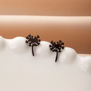 Detailed view of matte black dandelion stud earrings on a white ceramic display