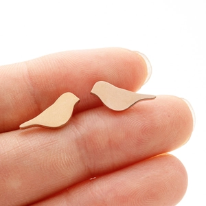Close-up of bird-shaped stainless steel earrings on fingertips showing actual product size