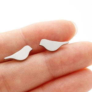 Close-up of minimalist bird stud earrings held on a fingertip to show small scale