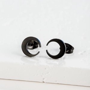 Detail of matte black moon stud earrings placed on a minimalist stone texture base