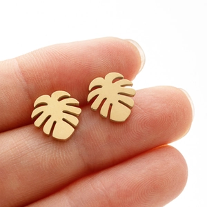 Macro detail of gold monstera leaf stud earring held on fingertip for size reference