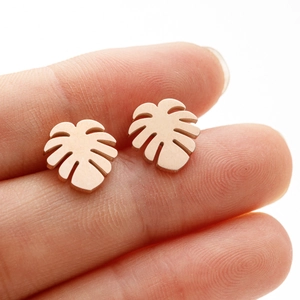 Detail of rose gold monstera leaf stud earrings with brushed metal finish held by hand