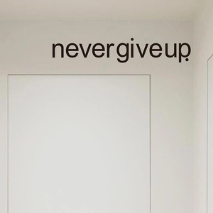 Close-up of black Never Give Up motivational wall decal on a clean white door frame