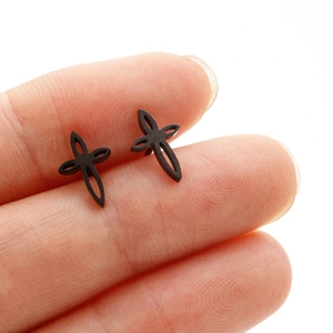 Détail des boucles d'oreilles croix noir mat tenues entre les doigts pour voir la taille
