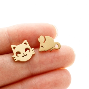 Detailed close-up of small golden asymmetric cat and mouse stud earrings on a fingertip