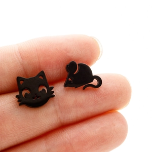 Detailed view of asymmetric matte black cat and mouse stud earrings held in hand
