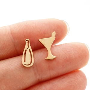 Macro shot of asymmetric gold wine bottle and glass studs held on a finger for scale