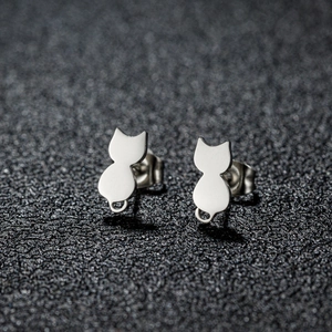 Macro shot of polished stainless steel cat-shaped stud earrings on a dark grey texture