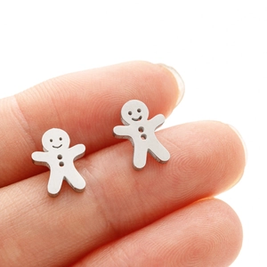 Close-up of small stainless steel gingerbread man stud earrings held against a fingertip