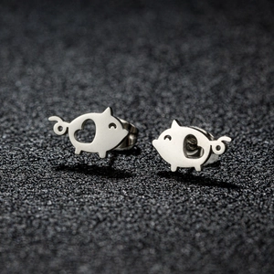 Macro shot of polished stainless steel pig stud earrings with heart-shaped cutouts on black surface