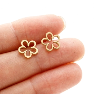 Detailed close-up of a tiny gold hollow flower earring held between fingers for scale