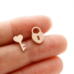 Detailed macro view of rose gold heart lock and key stud earrings held in hand