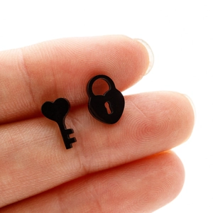 Macro shot of black stainless steel heart key and lock stud earrings held by hand
