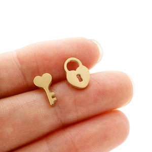 Close-up of tiny gold heart lock and key stud earrings held between fingertips