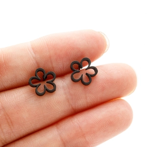 Close-up of minimalist black cutout flower stud earrings showing tiny scale on finger