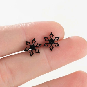 Close-up van zwarte sneeuwvlok oorknopjes met hol ontwerp vastgehouden tussen vingers