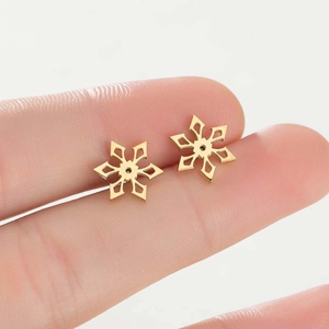 Detailopname van gouden sneeuwvlok oorknopjes op een vinger om de grootte aan te tonen