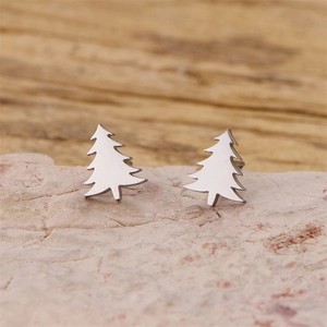Minimalist silver Christmas tree stud earrings displayed on a natural stone surface