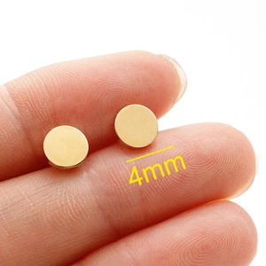 Polished 4mm gold circular stainless steel stud earrings held by fingers for scale
