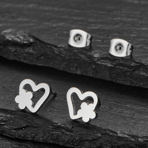 Polished stainless steel heart and flower stud earrings on a dark slate background