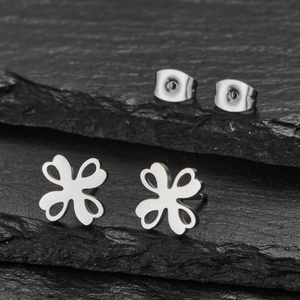 Polished silver stainless steel clover stud earrings with hollow design on rock background