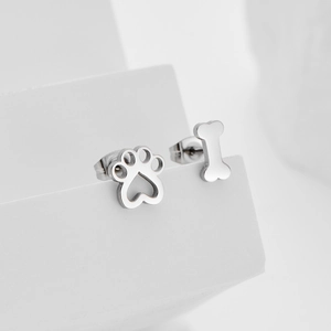 Asymmetrische silberne Katzenpfoten und Knochen-Ohrstecker auf minimalistischem Sockel
