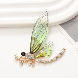 Elegante spilla a libellula dorata con ali verdi e cristalli su fondo bianco