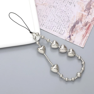 Silver metallic heart beaded phone strap with Y2K aesthetic hanging on a decorative plate